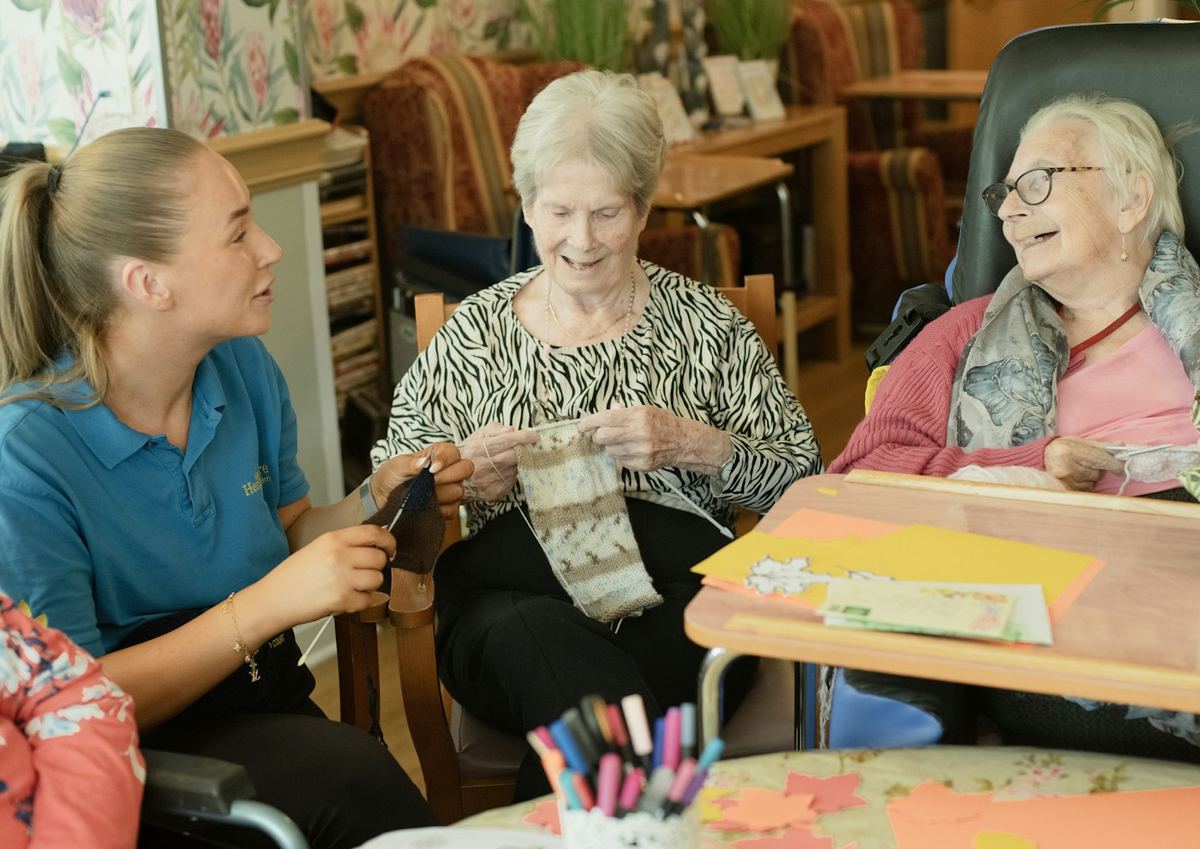 A caregiver helping two older women with a knitting project